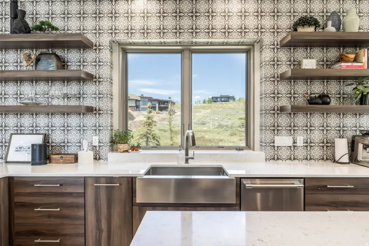Patterned tile backsplash, floating wood-finish shelves, under-mount stainless steel sink, stainless steel dishwasher, and light-toned countertops