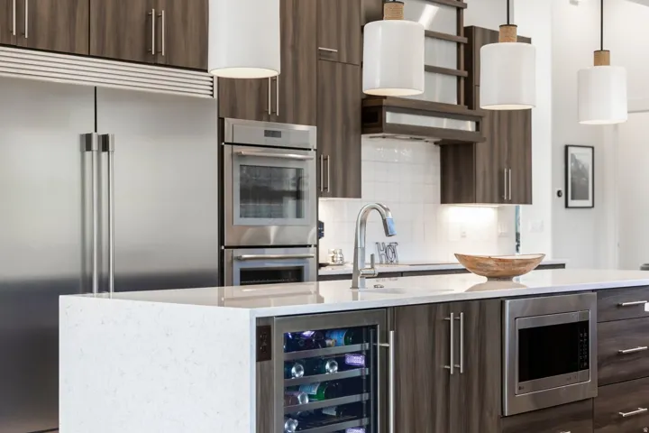 Kitchen featuring stainless steel appliances, wood-finish cabinetry, a white subway tile backsplash, a kitchen island with a built-in wine refrigerator, and pendant lighting