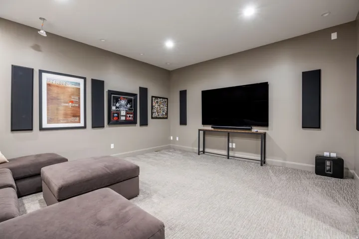 Recessed ceiling lighting, wall-mounted sound panels, light-colored patterned carpeting, and a console table with a wood-finish top