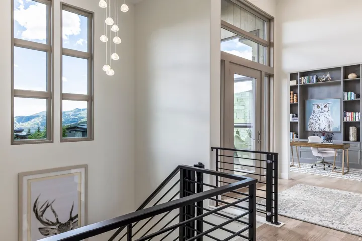 Double-height entry with a multi-pane window, suspended light fixture, black metal railing, and wood-finish flooring