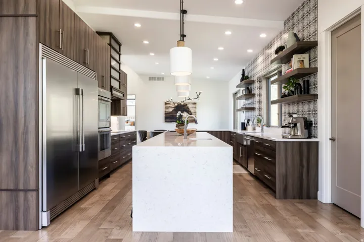 Gourmet kitchen featuring a large central island, stainless steel appliances, wood-finish cabinetry, patterned accent wall, and wood-finish flooring