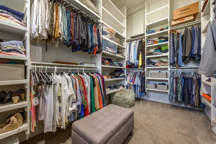 Built-in closet system featuring extensive shelving, multiple hanging rods, corner shelving, and carpet flooring