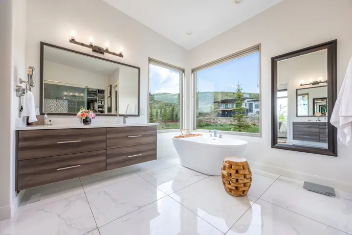 Freestanding soaking tub, dual floating vanity with white countertops, white tile flooring, and large windows