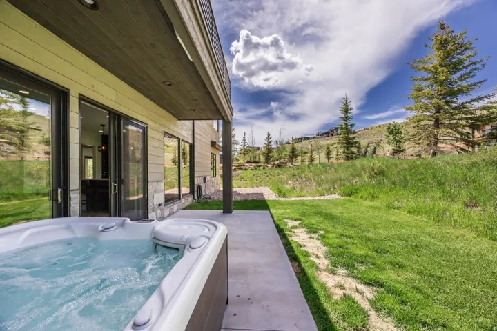 Outdoor spa with a concrete patio, sliding glass doors, stone veneer accents, and a grassy hillside