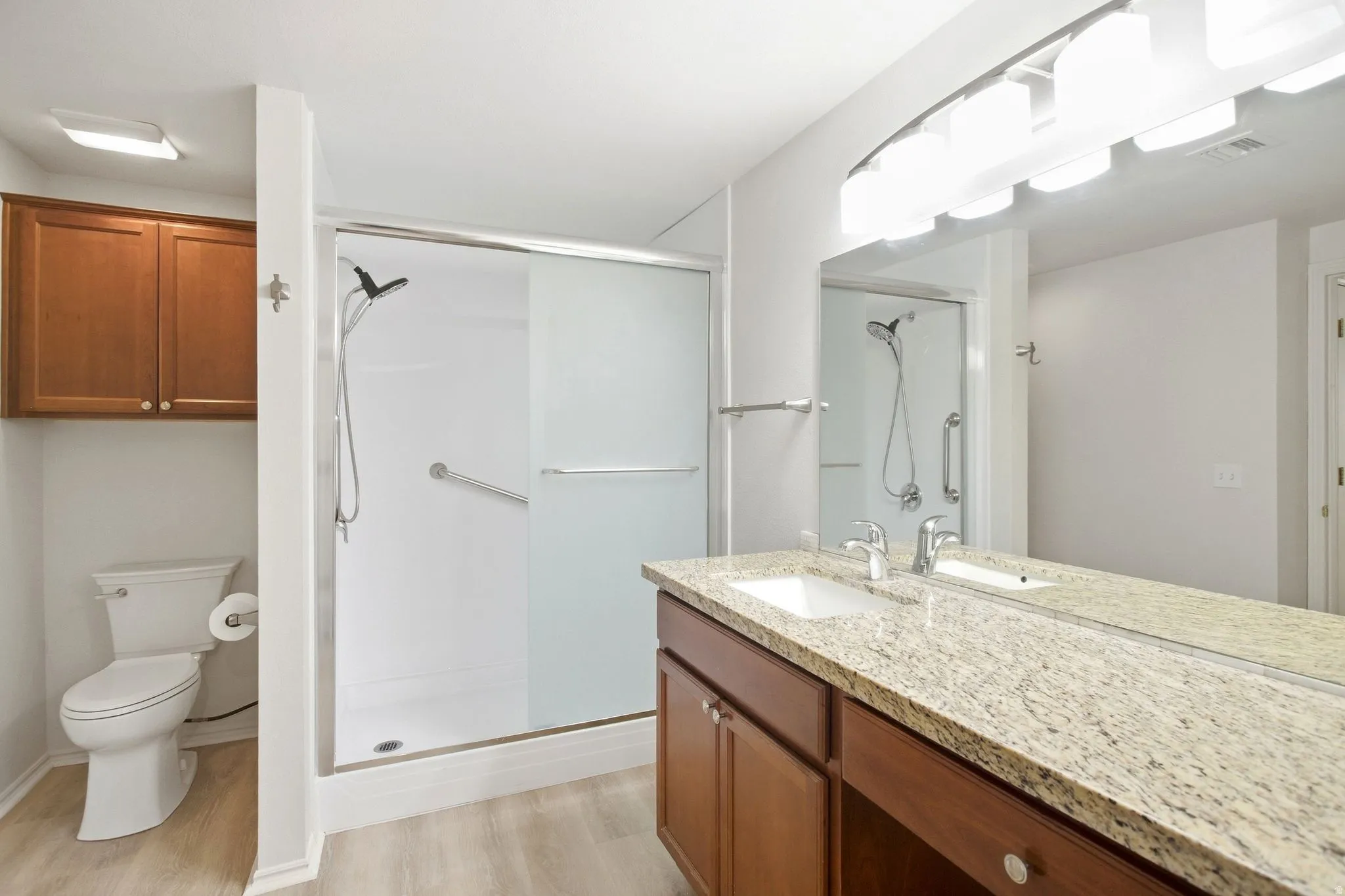 Granite-finish vanity with an integrated sink, expansive mirror, wood-finish cabinetry, and a walk-in shower with a sliding glass door