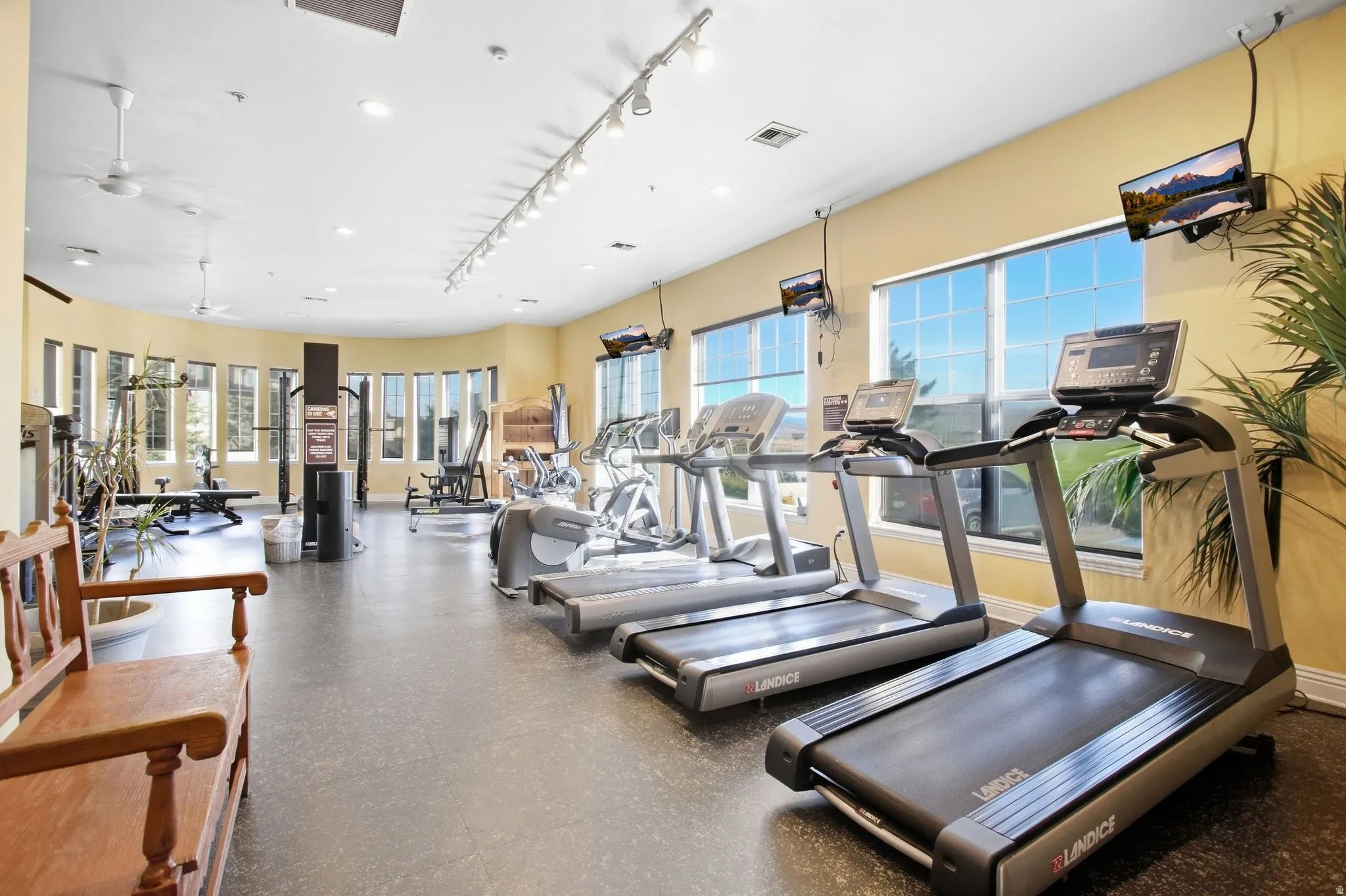 Fitness center featuring durable flooring, multiple windows, ceiling fans, track lighting, and mounted televisions