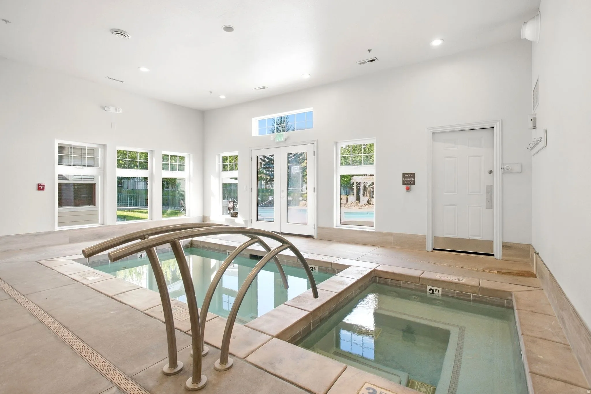 Indoor aquatic facility featuring two in-ground spas, tiled surrounds, and multiple windows allowing natural illumination