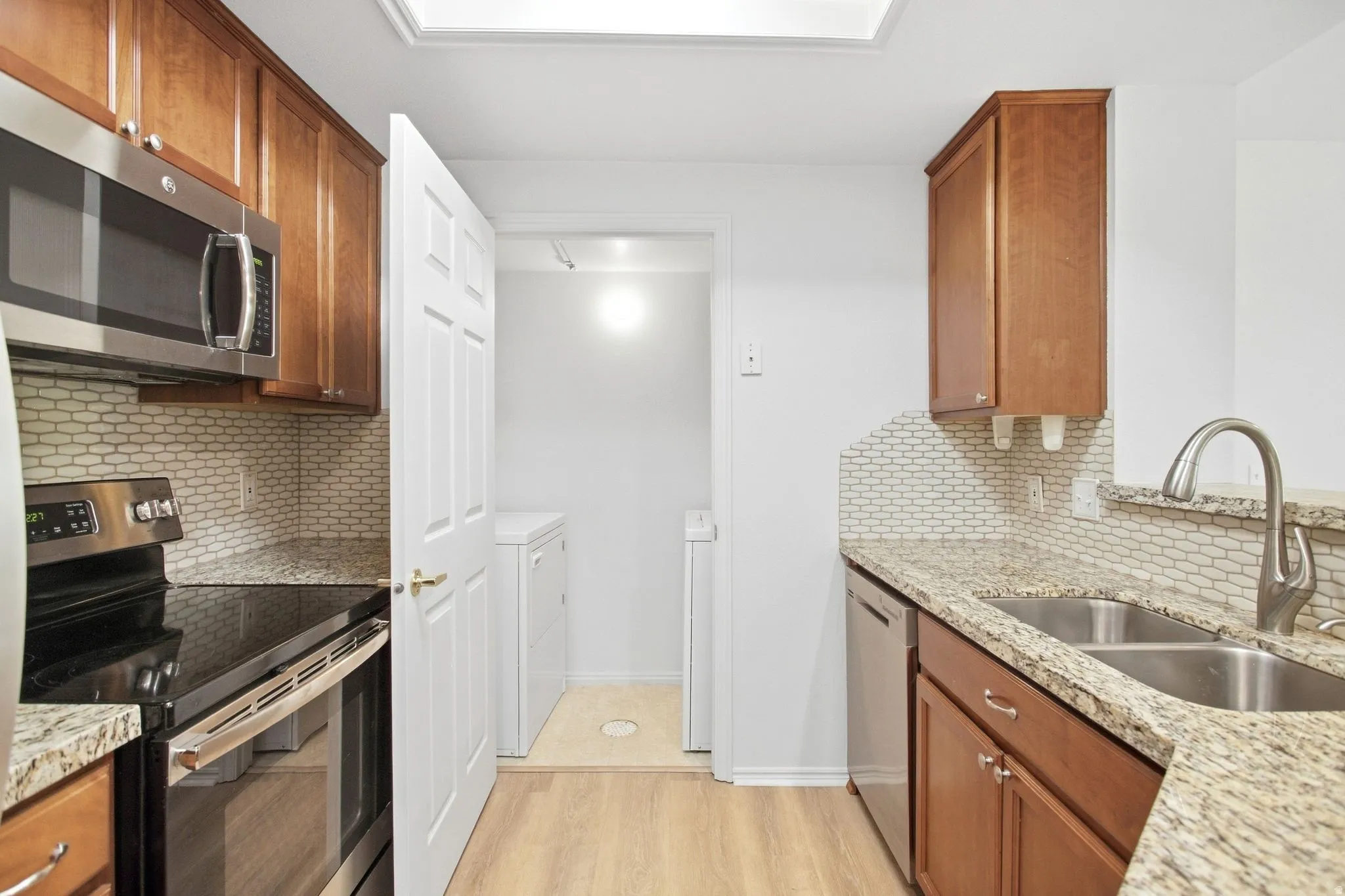 Kitchen featuring wood-finish cabinetry, light-toned granite countertops, and a full stainless steel appliance package including a built-in microwave, range, and dishwasher