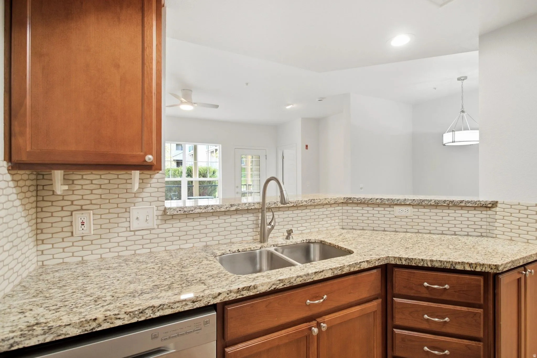 Kitchen featuring wood cabinetry, a double basin sink with a gooseneck faucet, light-toned stone countertops, and a patterned tile backsplash