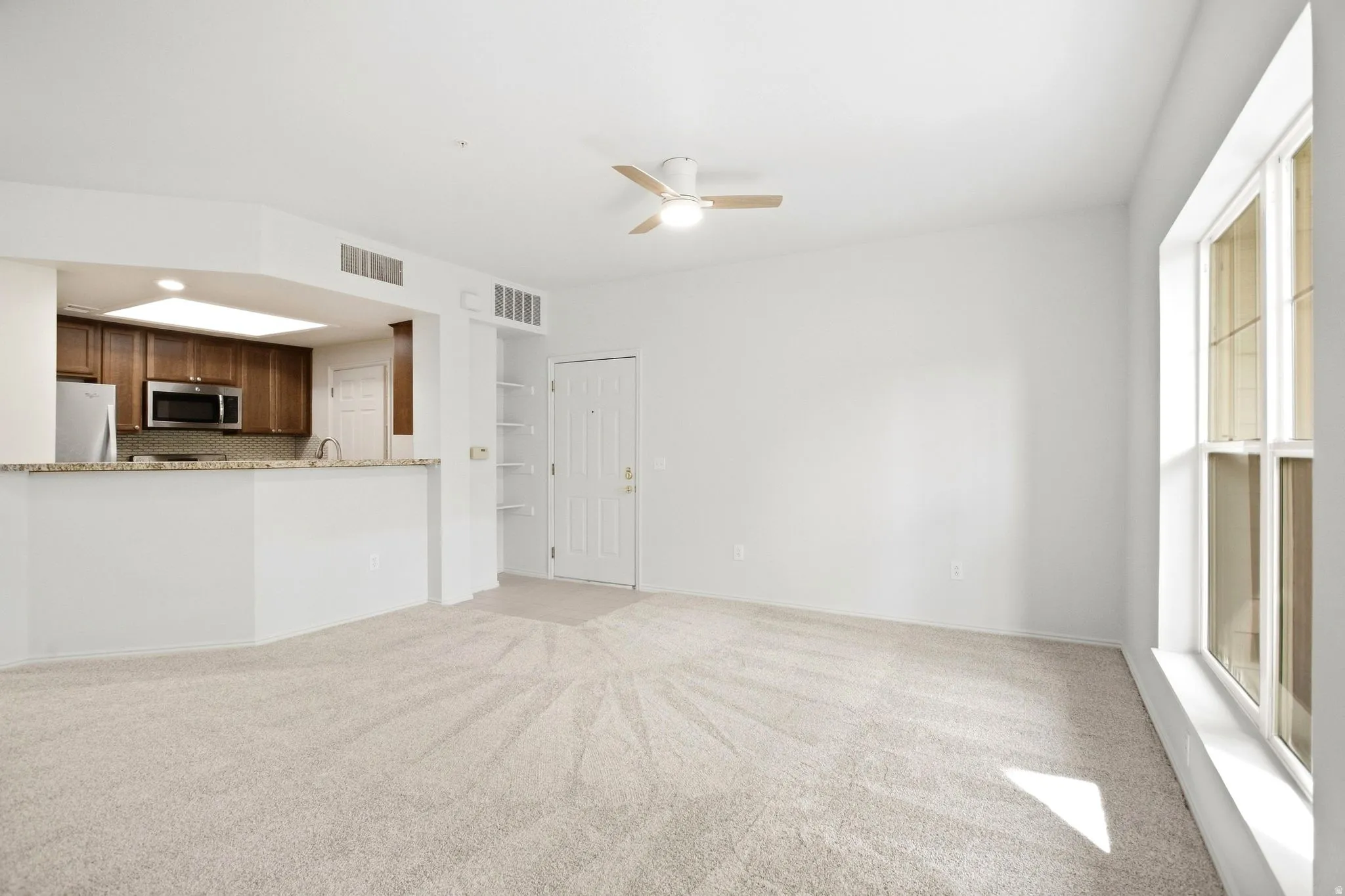 Living area with light-toned carpeting, a ceiling fan, and a large window