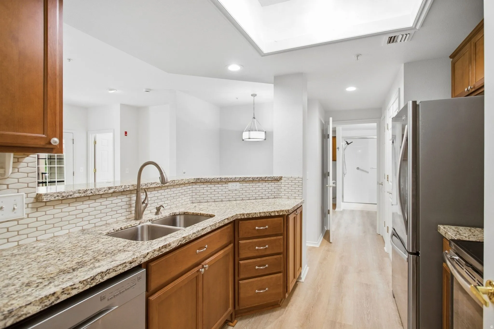Kitchen featuring dual basin stainless steel sink, granite countertops, wood-finish cabinetry, stainless steel appliances, and a subway tile backsplash