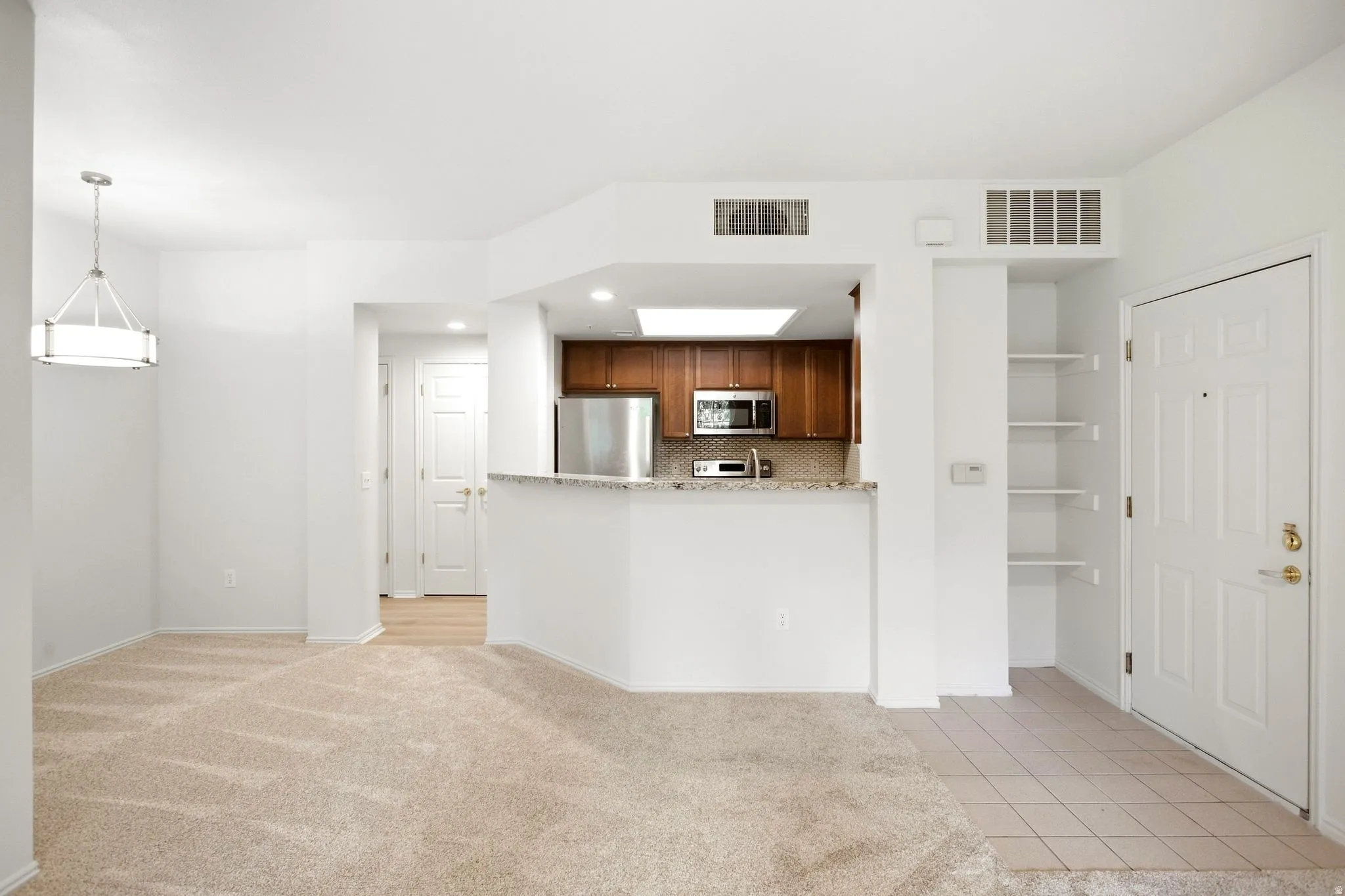 Open-concept living area with neutral carpeting, kitchen featuring wood cabinetry and stainless steel appliances, and a dedicated entry space with built-in shelving