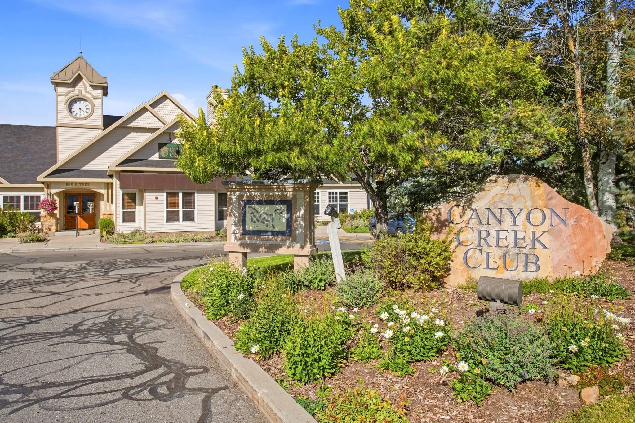 Community entrance featuring a stone monument with carved lettering, manicured landscaping, and mature trees