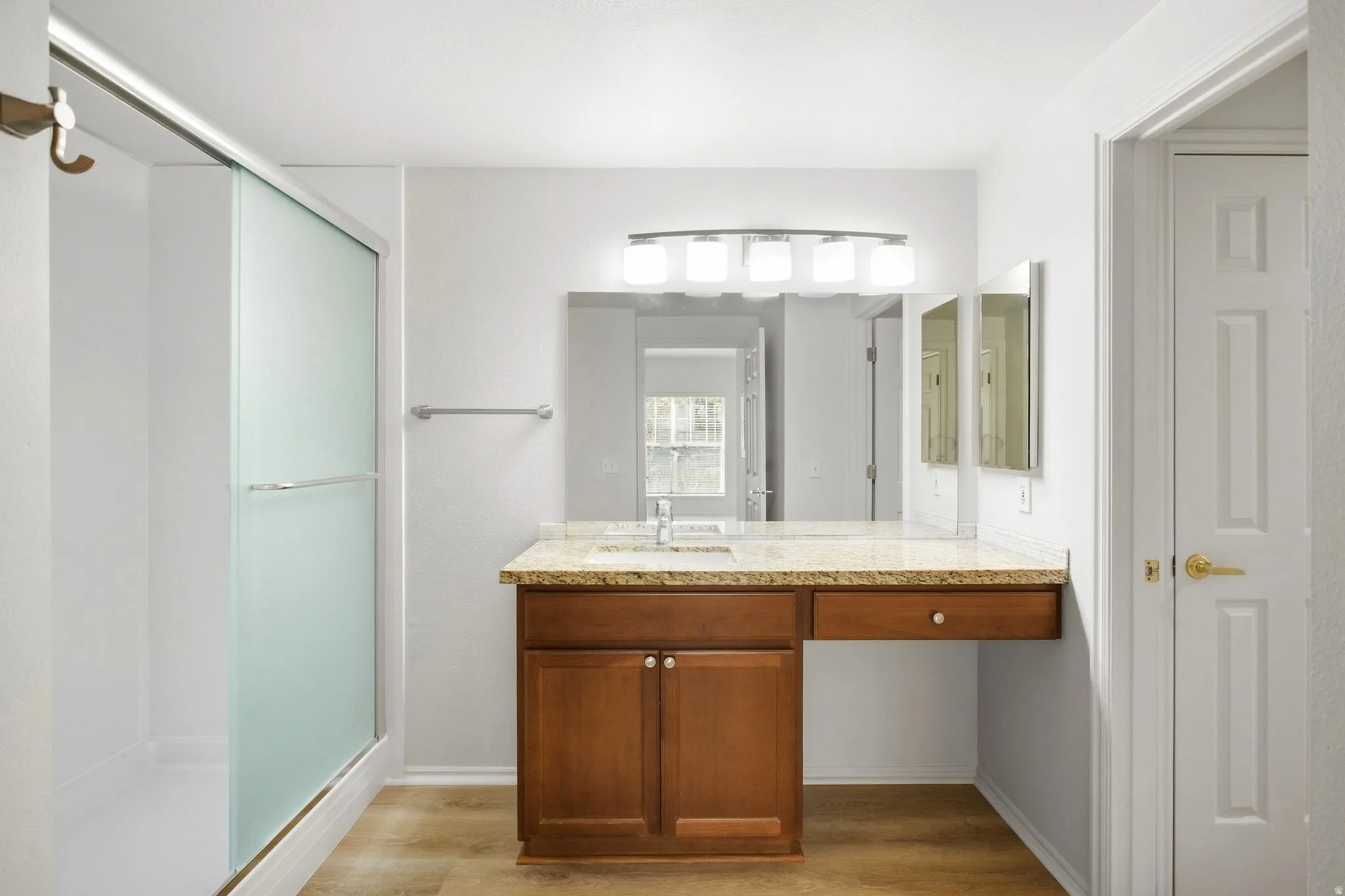 Frosted glass shower enclosure, wood-finish flooring, vanity with stone-finish countertop, integrated single basin sink, and wood cabinetry