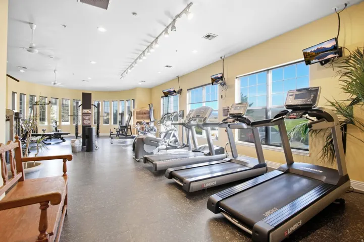 Fitness center featuring durable flooring, multiple windows, ceiling fans, track lighting, and mounted televisions