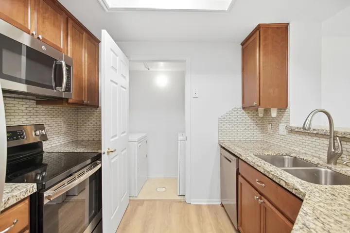 Kitchen featuring wood-finish cabinetry, light-toned granite countertops, and a full stainless steel appliance package including a built-in microwave, range, and dishwasher
