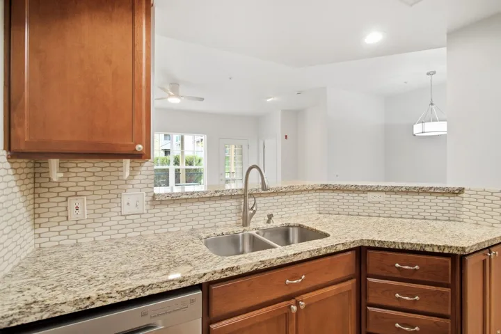Kitchen featuring wood cabinetry, a double basin sink with a gooseneck faucet, light-toned stone countertops, and a patterned tile backsplash