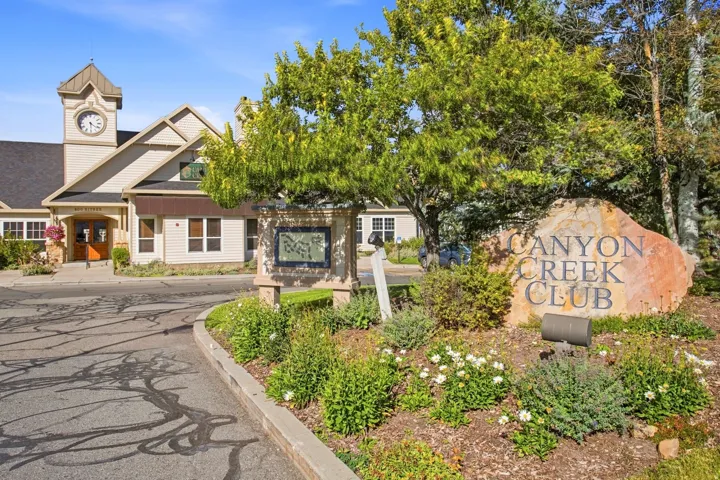 Community entrance featuring a stone monument with carved lettering, manicured landscaping, and mature trees