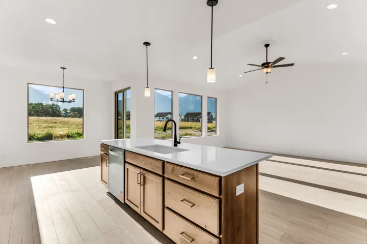 Wood-finish flooring throughout, kitchen island with built-in sink and dishwasher, white countertops, multiple pendant lights, and a ceiling fan