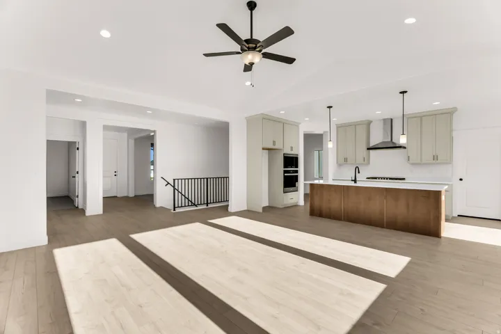 Open-concept living area featuring wood-finish flooring, a contemporary ceiling fan, and a kitchen with an island, pendant lighting, and stainless steel appliances