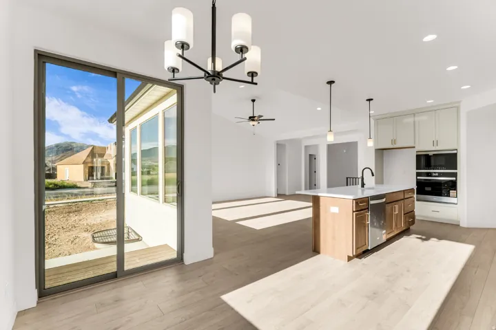 Open-concept living space featuring wood-finish flooring, a kitchen island with integrated sink, stainless steel appliances, and a sliding glass door leading to an outdoor area
