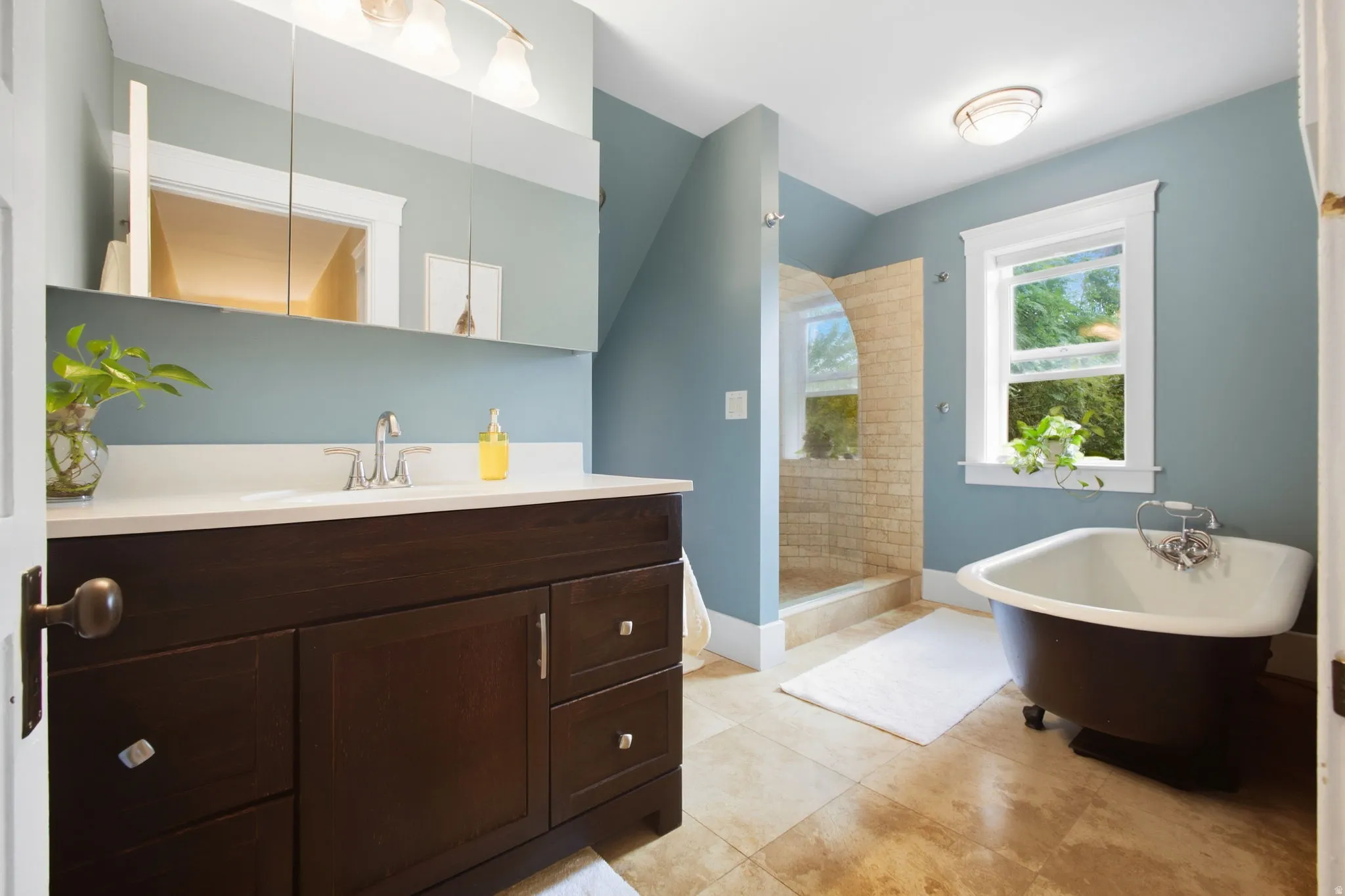 Dark wood-finish vanity with white countertop, chrome faucet, and travertine tile.