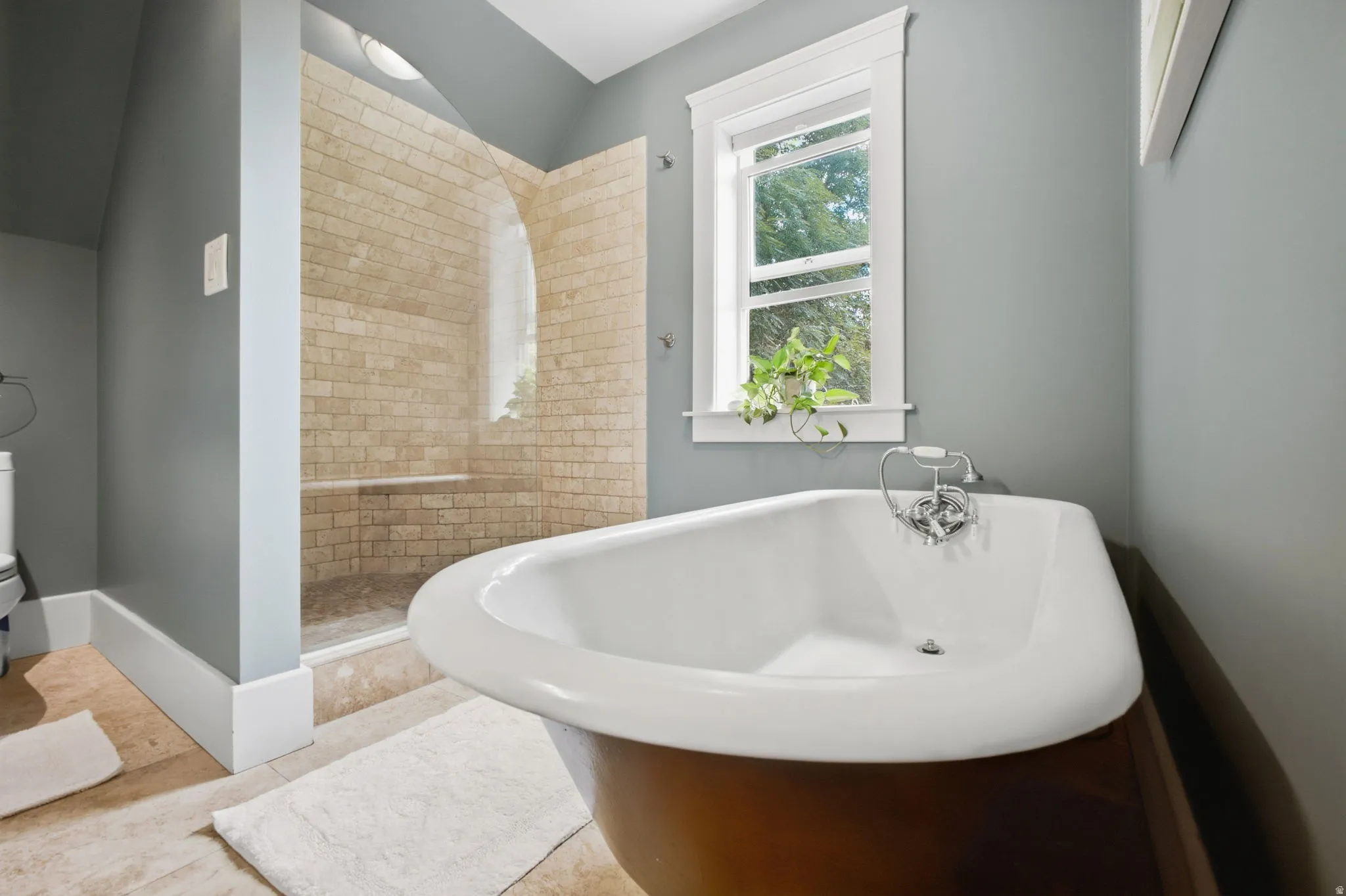 Freestanding stunning claw foot bathtub with chrome fixtures, custom tiled shower with integrated bench, and a single-pane window.