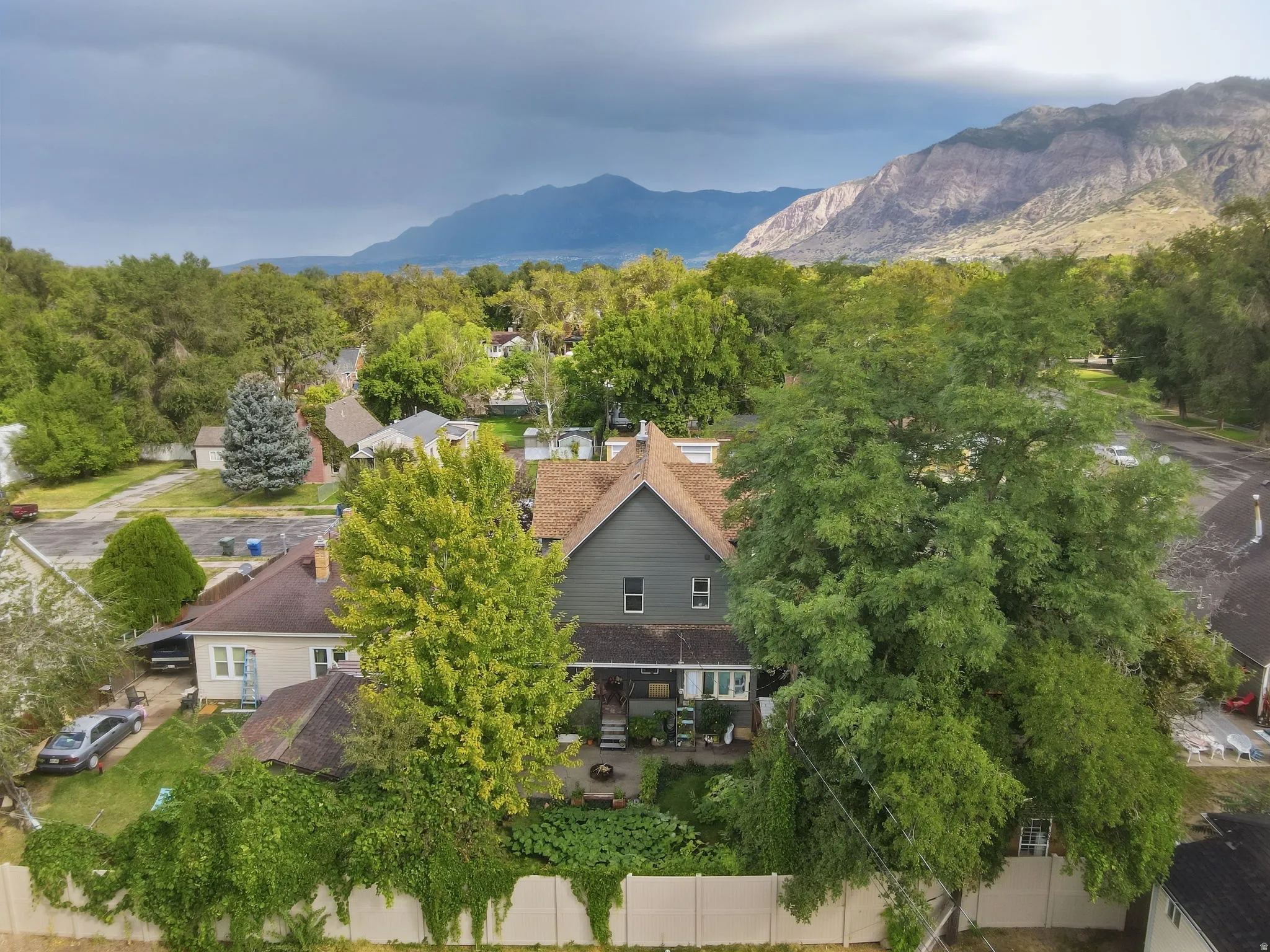 Property featuring a gabled roof, mature trees, a private fenced yard, and a paved outdoor patio area.
