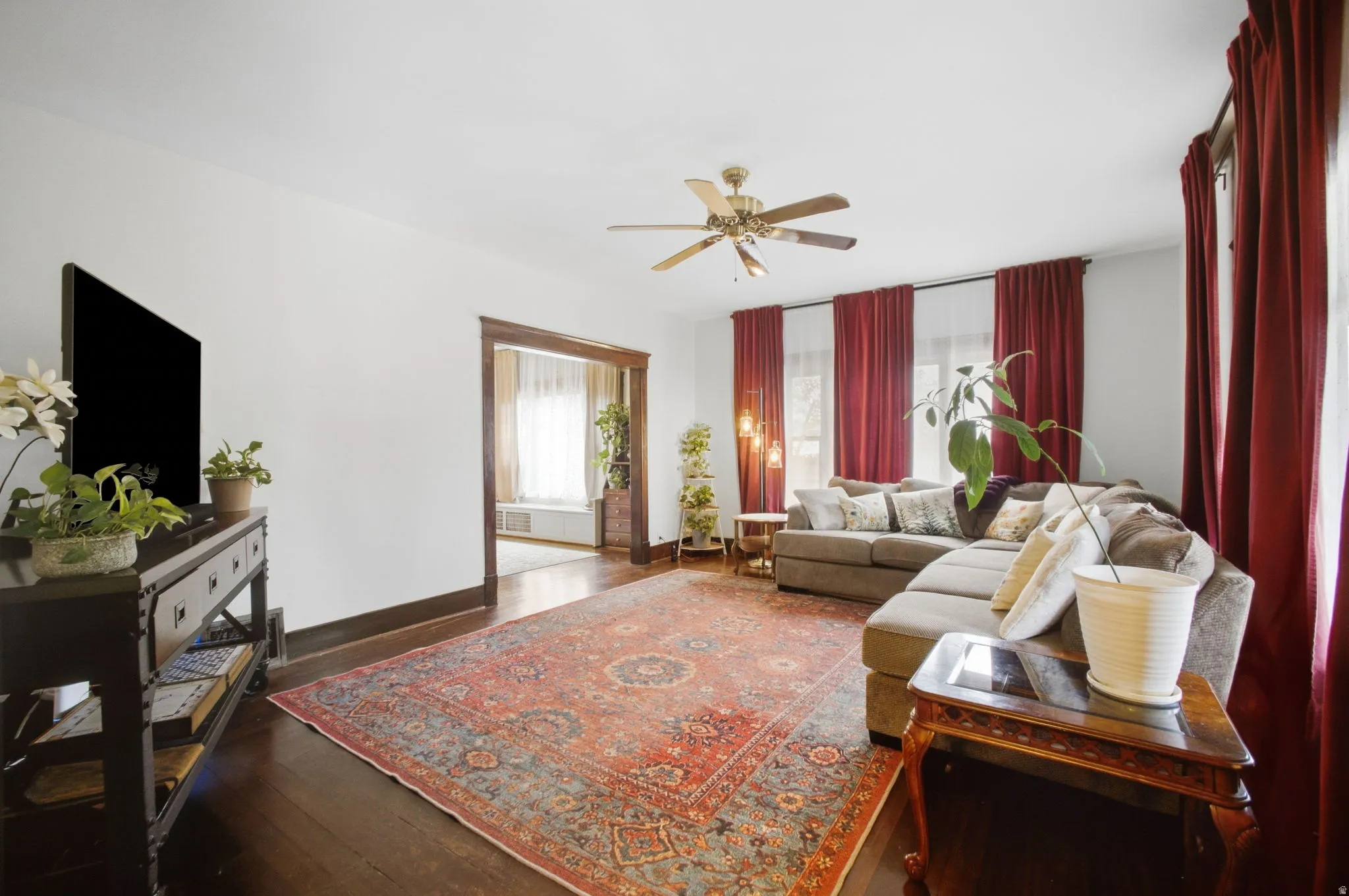 Large living room with dark wood-finish flooring, original dark wood trim, 9' ceiling, white painted walls, and a ceiling fan.