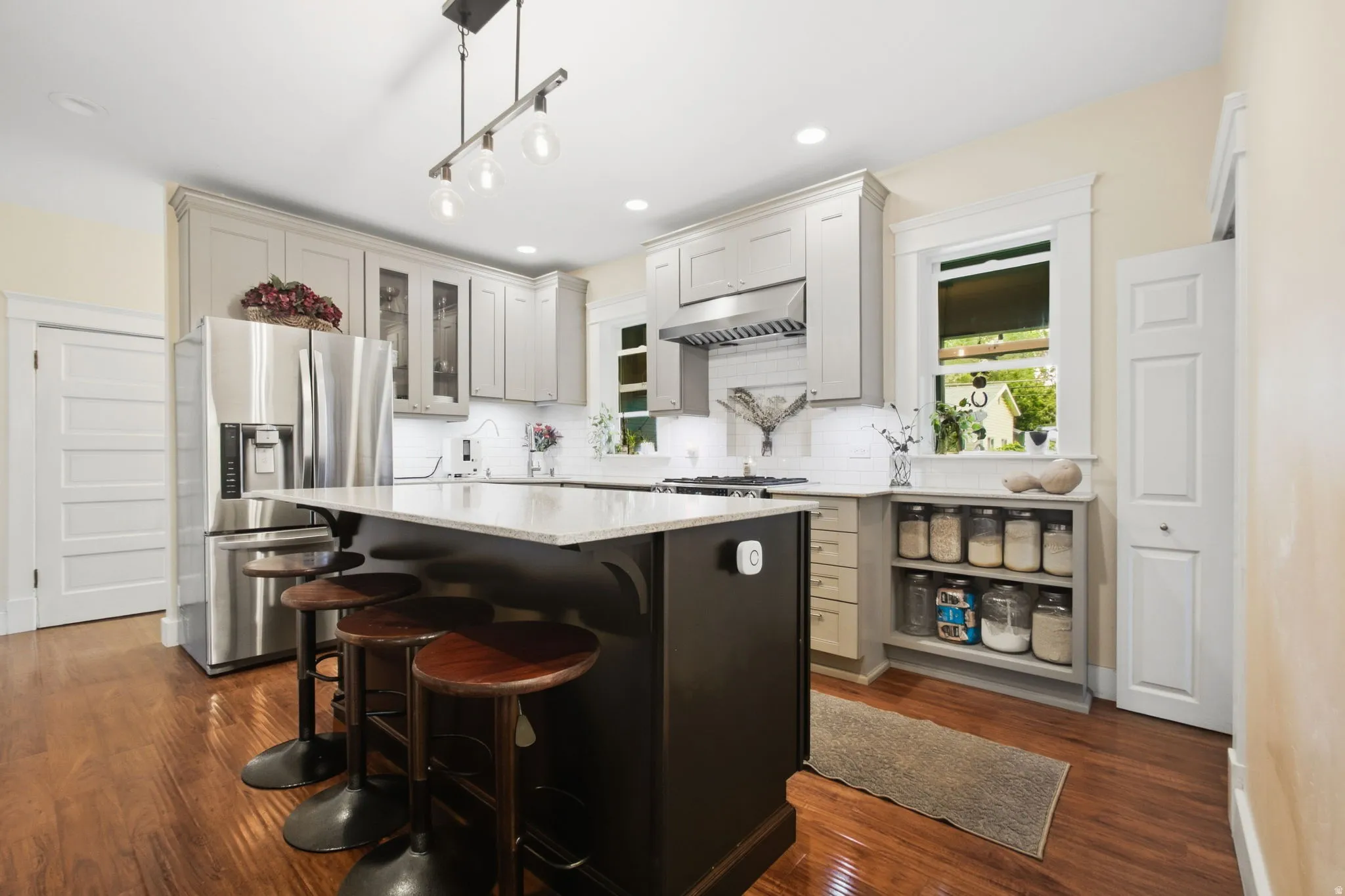 Wood finish flooring, stainless steel appliances, large kitchen island with counter seating, light toned cabinetry, recessed and decorative lighting.