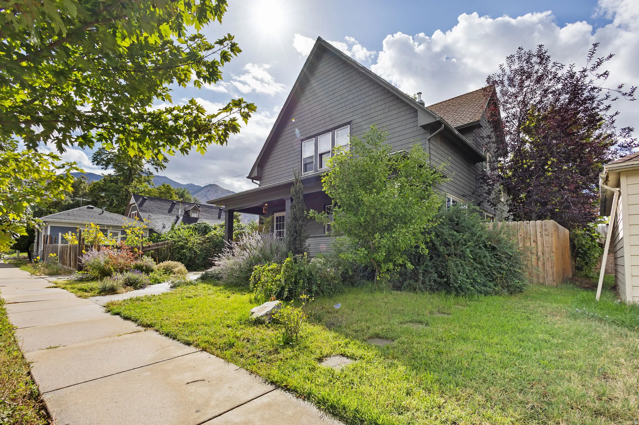 Gabled roofline with a covered front porch, featuring exterior siding and a manicured front lawn with mature trees.