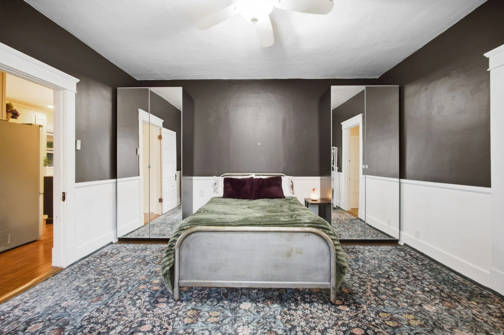 First floor bedroom with white wainscoting, a rich dark wall finish, and mirrored closets.