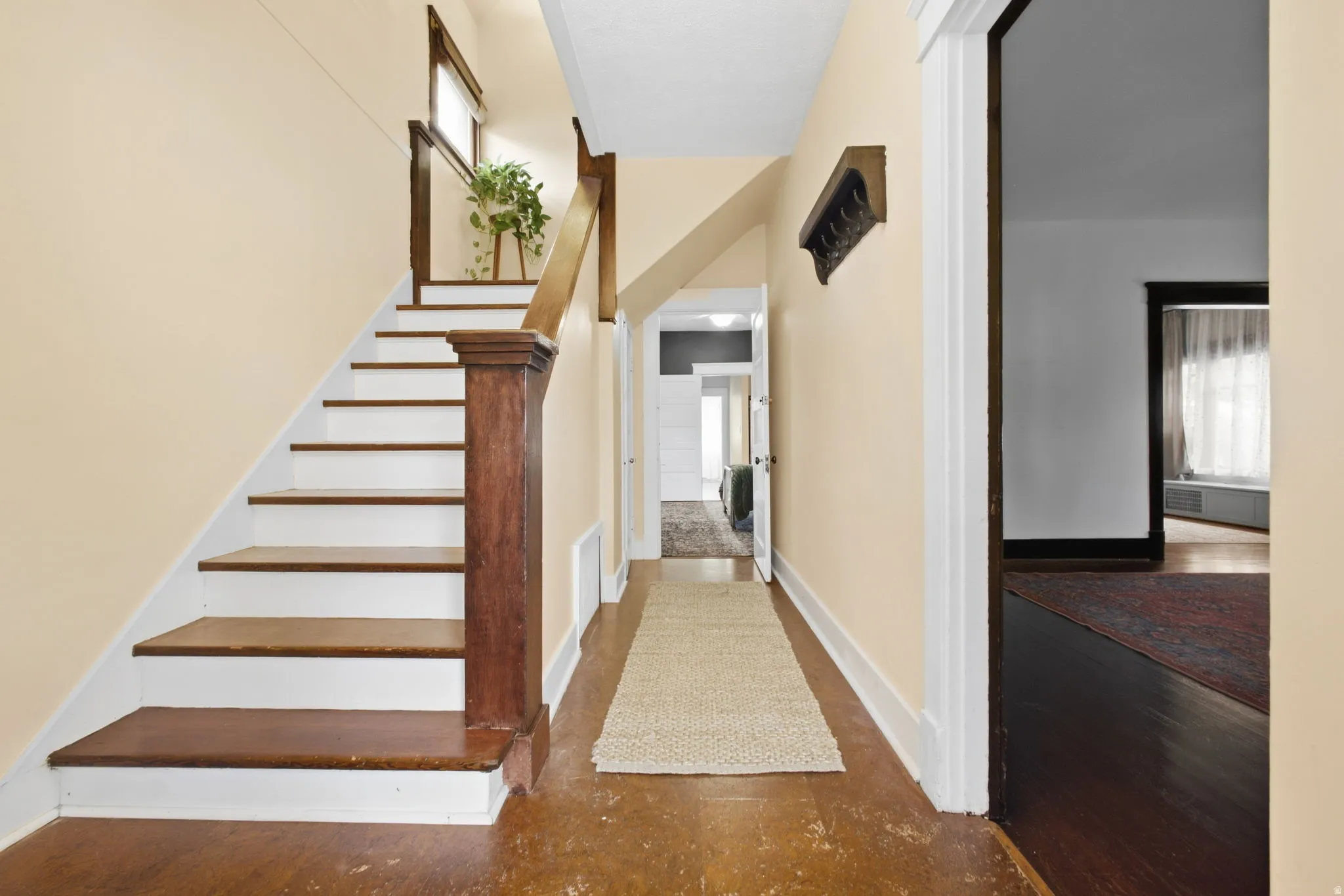 Wood-finish flooring throughout, white risers on a wood staircase, natural wood newel post and handrail, light-colored wall paint, and white trim.