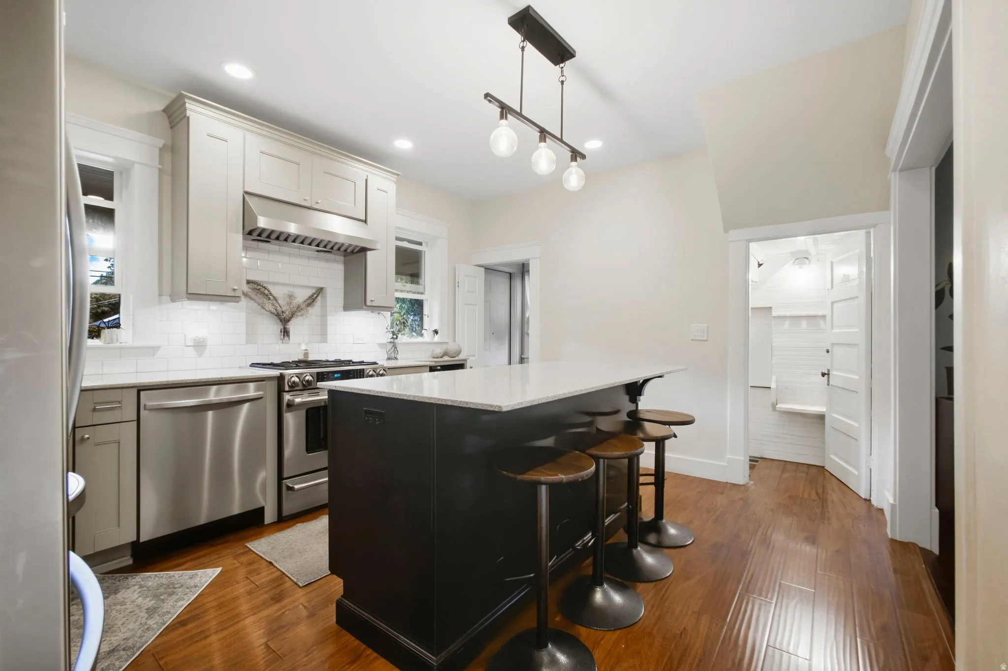 Kitchen featuring a center island with stainless steel hood range, white subway tile backsplash, windows for natural light and it is open to the dining room and living room.
