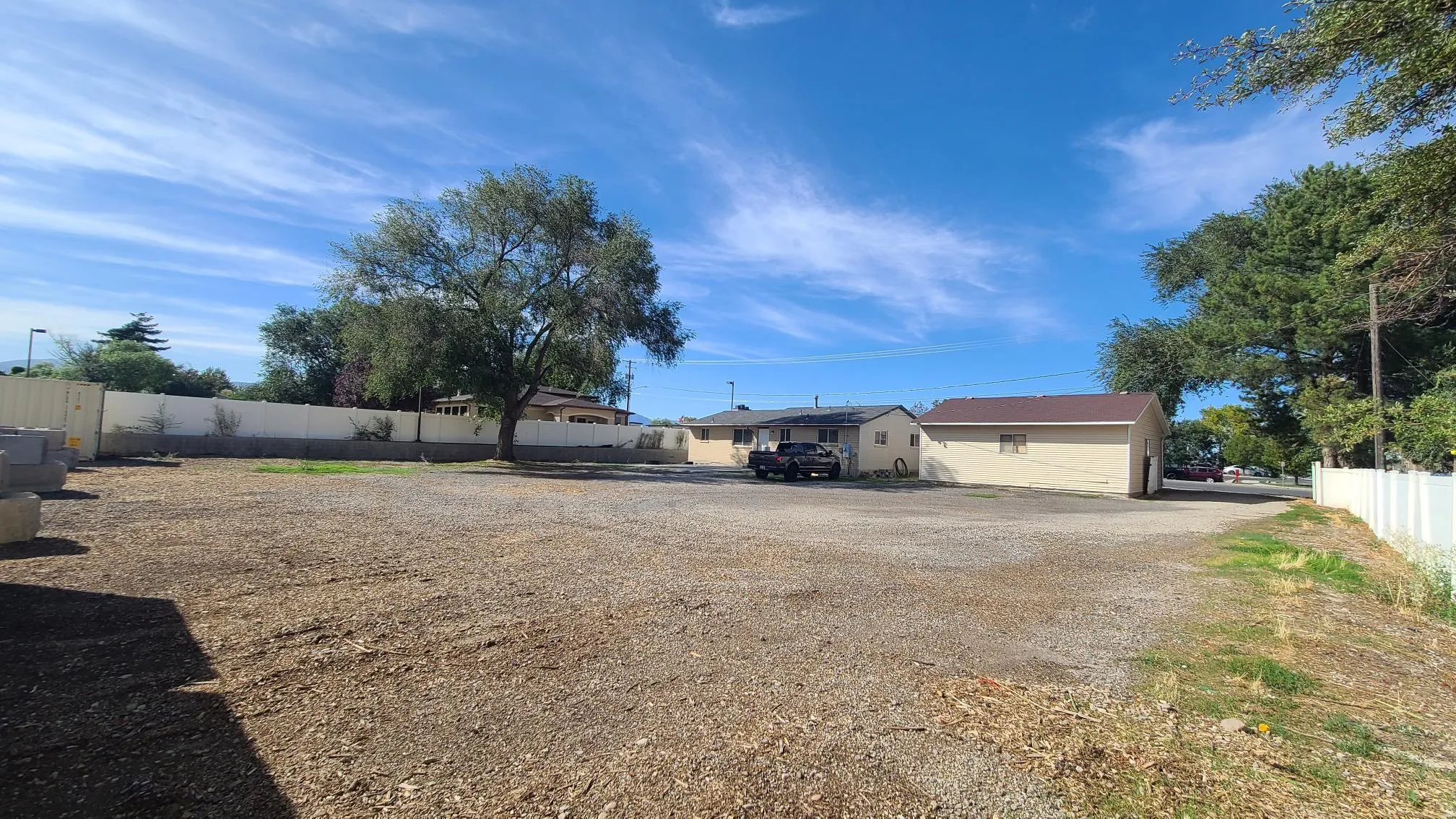 Expansive gravel lot with mature trees and perimeter fencing