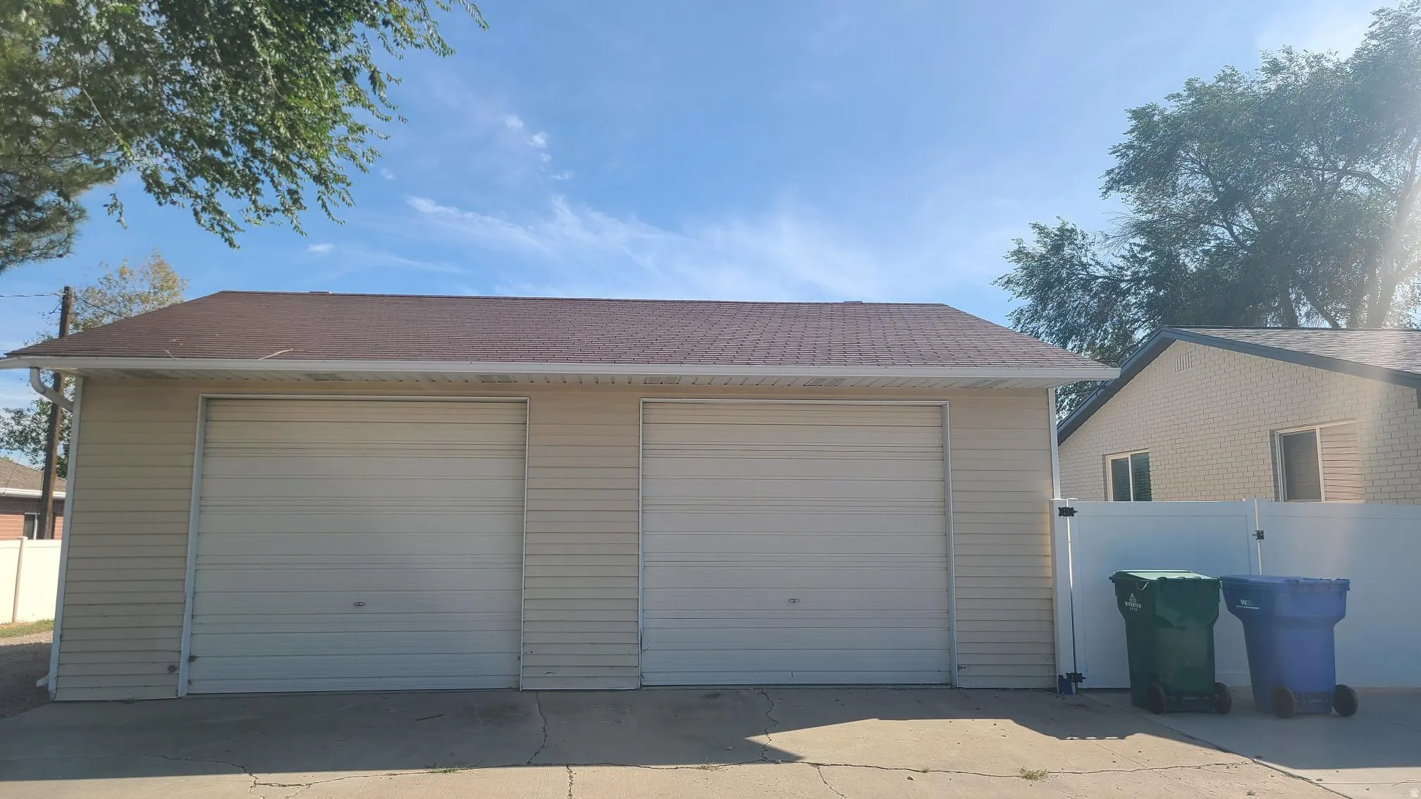 Detached two-car garage with light-colored siding and a brown shingle roof