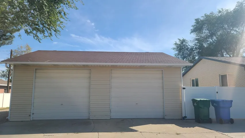 Detached two-car garage with light-colored siding and a brown shingle roof