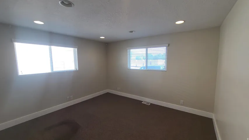 Recessed lighting, neutral wall paint, two windows with blinds, and dark carpet flooring
