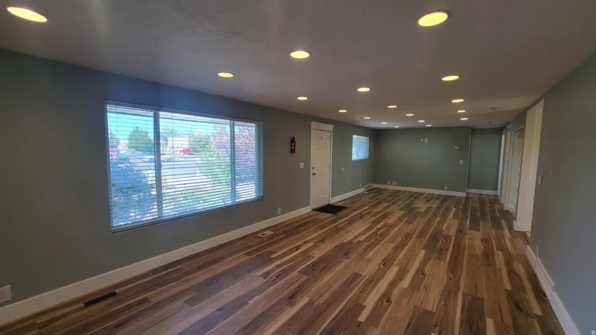 Wood-finish flooring, recessed ceiling lighting, light gray wall paint, and multiple windows with blinds