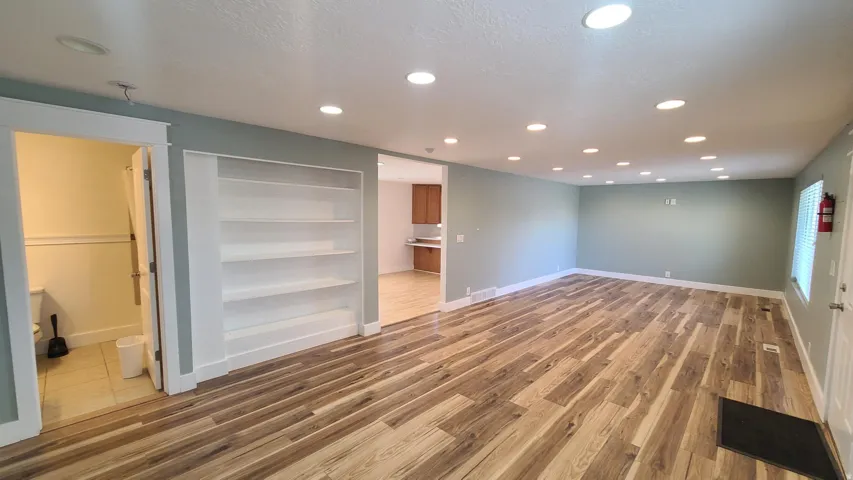 Wood-finish flooring throughout, recessed ceiling lighting, built-in shelving, and a neutral wall color palette