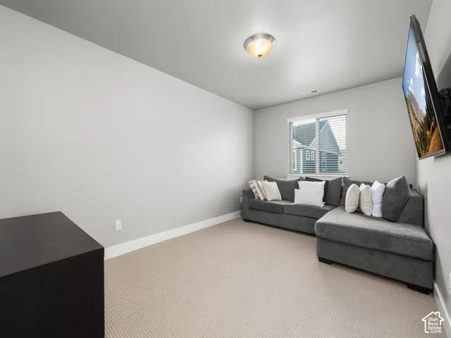 Carpeted room featuring a single window with blinds, a wall-mounted light fixture, light gray walls, and white baseboards