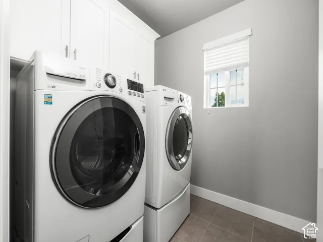 Laundry area featuring a window with white blinds, white upper cabinetry with brushed nickel hardware, and tile flooring