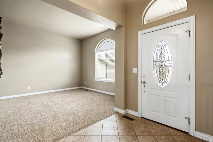 Entryway featuring a white door with decorative glass, tiled flooring, and an arched transom window