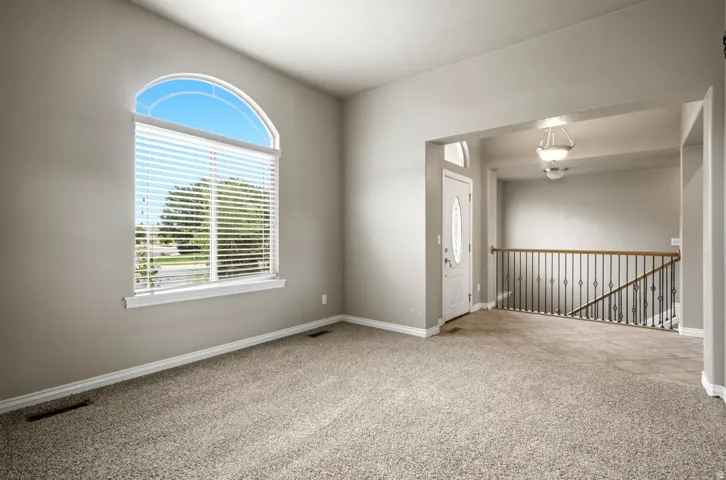 Arched window with blinds, carpeted flooring, white entry door with oval glass insert, wrought iron railing, and recessed lighting