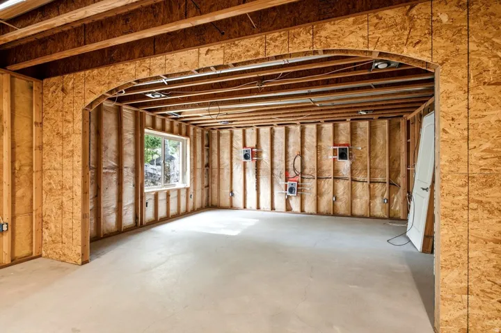 Framed interior with an arched entryway, exposed ceiling joists, and a window providing natural light