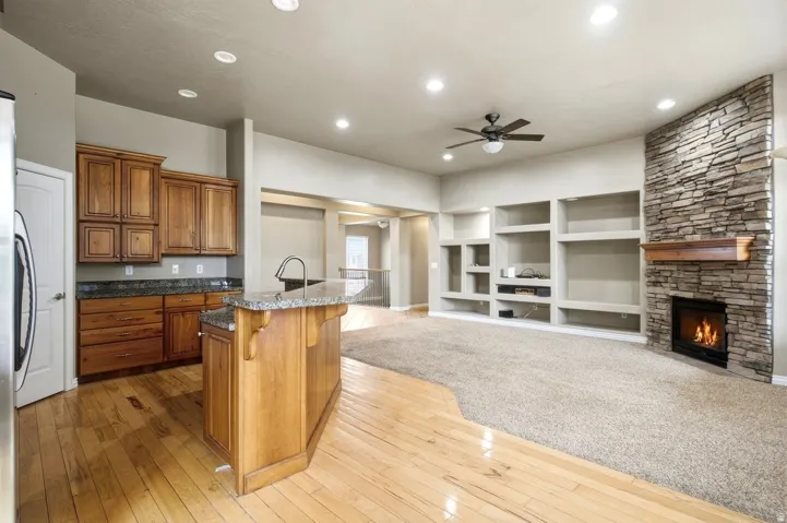 Wood-finish flooring, granite countertop island, natural stone fireplace, built-in shelving, and recessed lighting