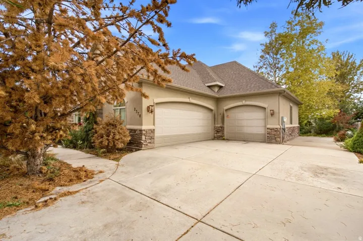Stucco exterior with stone accents, two-car garage, single-car garage, paved driveway, and established landscaping