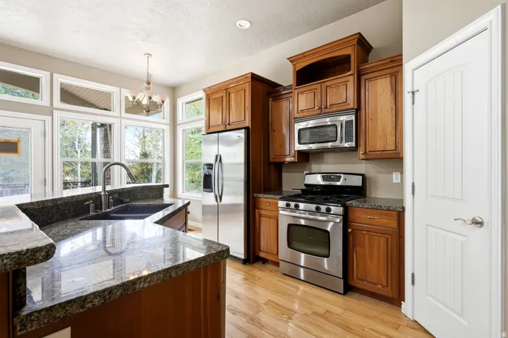 Kitchen featuring wood-finish cabinetry, stainless steel appliances, granite countertops, and wood-finish flooring