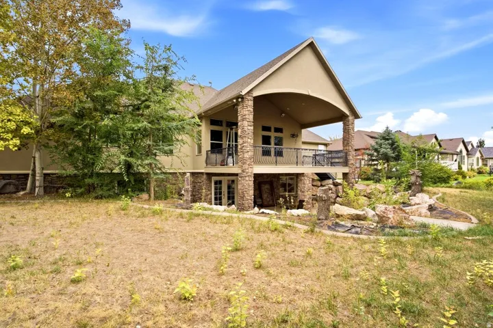 Multi-level exterior featuring a covered patio with a metal railing and stone columns, a lower-level French door entry, and a rock garden