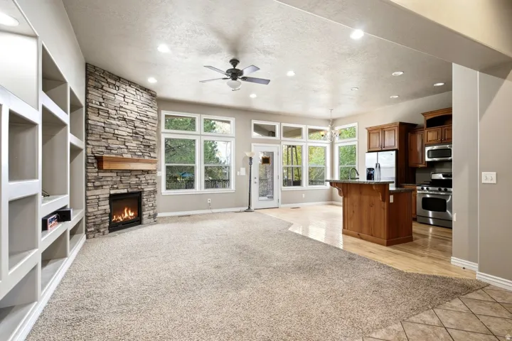 Stone-clad fireplace with wood mantle and hearth, built-in shelving, ceiling fan, and recessed lighting
